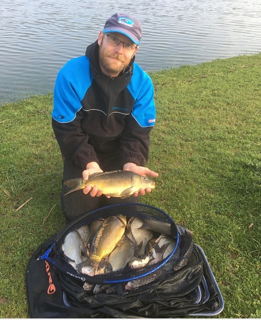 homme avec un poisson dans les mains et une bourriche pleine de poissons à ses genoux